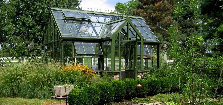 Green glass greenhouse in a garden with hedges and flowers