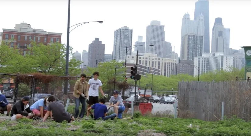 Group of people gathered at an urban farm lot with a city skyline behind them