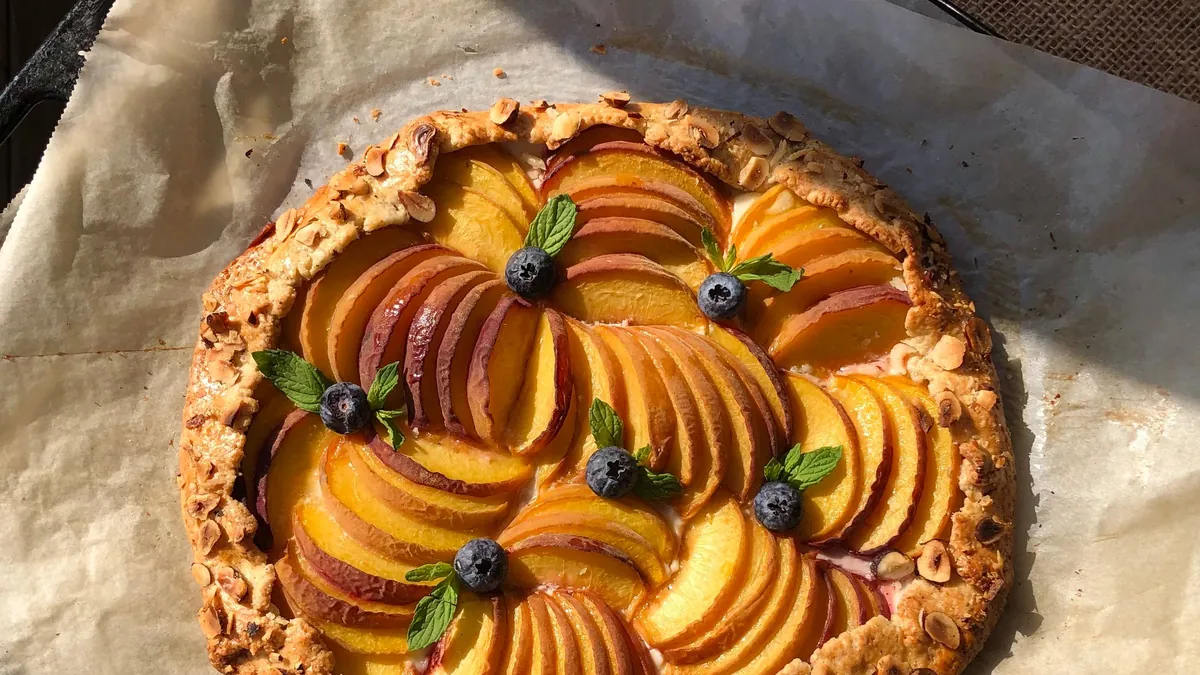 Peach galette topped with blueberries and mint on parchment paper