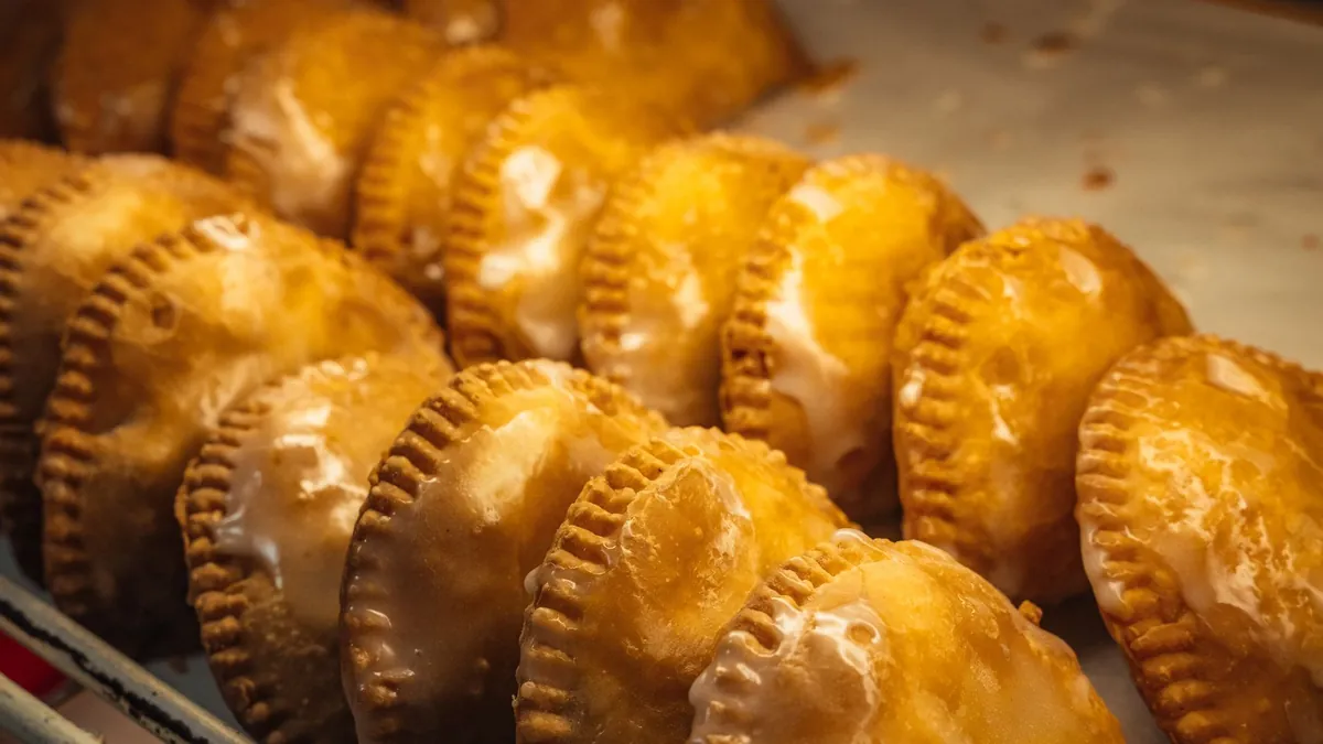 Rows of golden glazed hand pies on a bakery tray