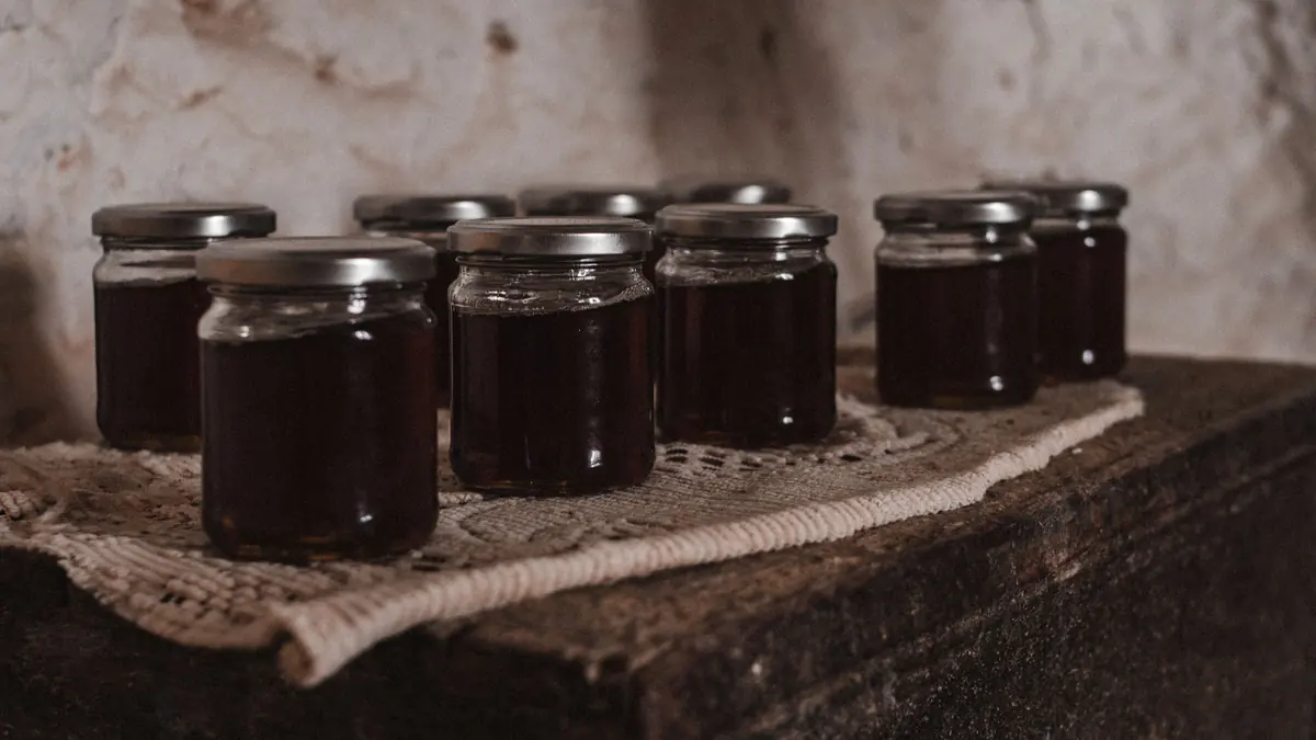 Glass jars of dark homemade fruit preserves on a rustic wooden table