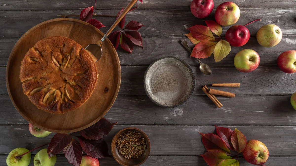 An apple pie on a dark wooden table among apples, autumn leaves and cinnamon sticks