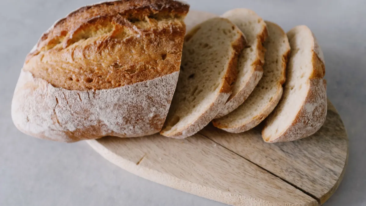A crusty loaf of bread with several slices on a wooden board
