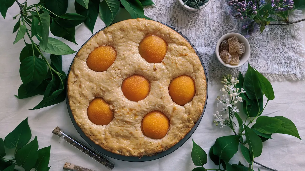A round fruit pie topped with apricot halves beside green leaves and flowers