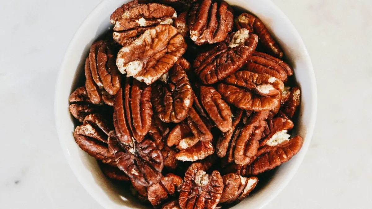 White bowl of shelled pecans on a light surface