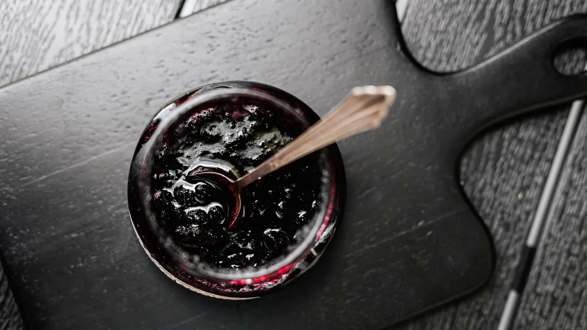 Dark berry jam in a glass jar with a spoon