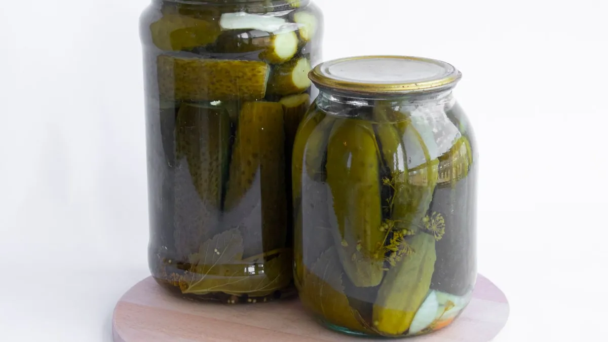 Two glass jars of pickled cucumbers on a wooden board