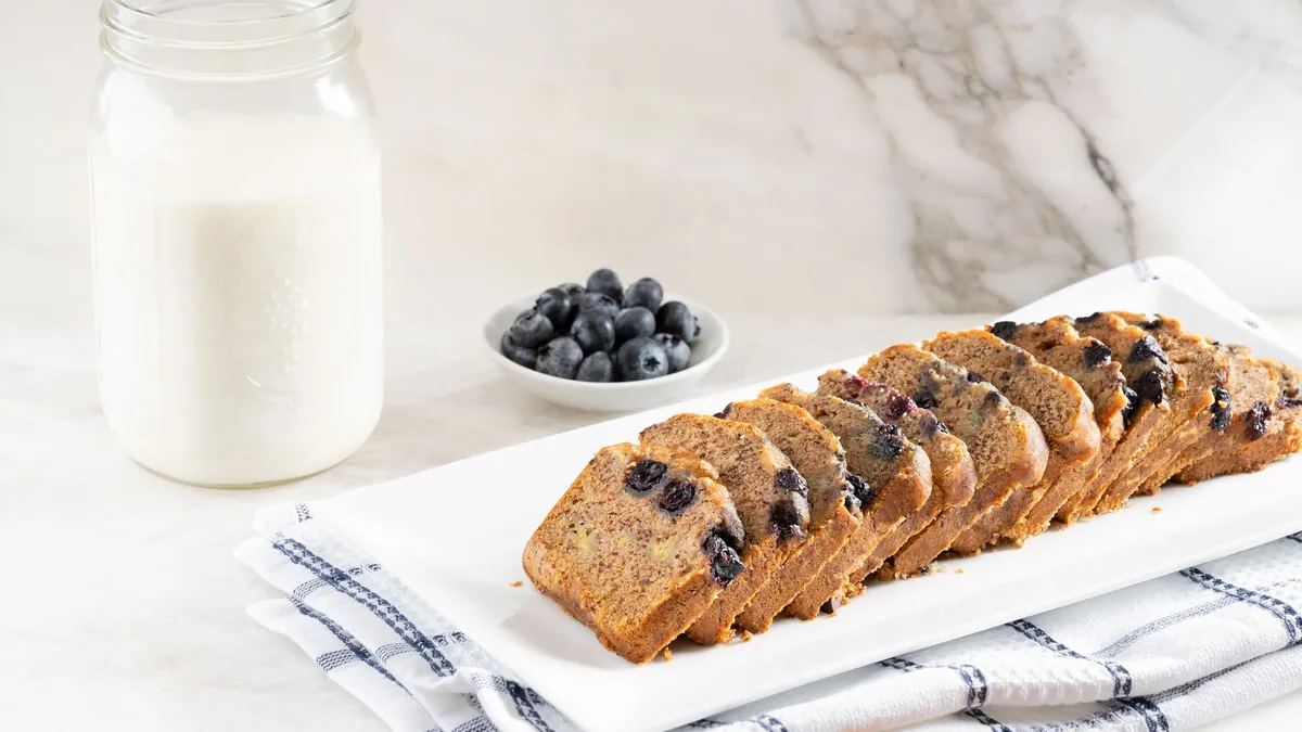 Sliced blueberry bread on a white plate beside a jar of milk