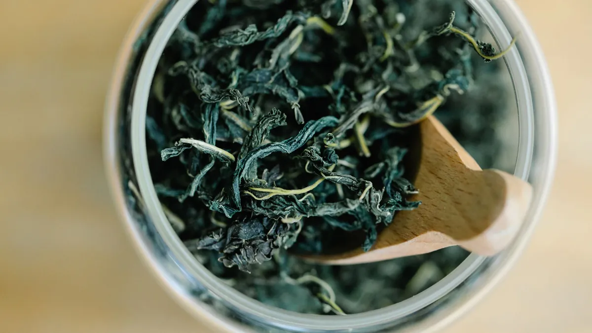 Dried tea leaves in a glass jar with a wooden scoop