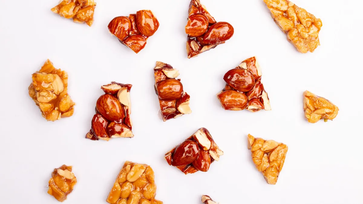 Pieces of peanut and almond brittle scattered on a white surface