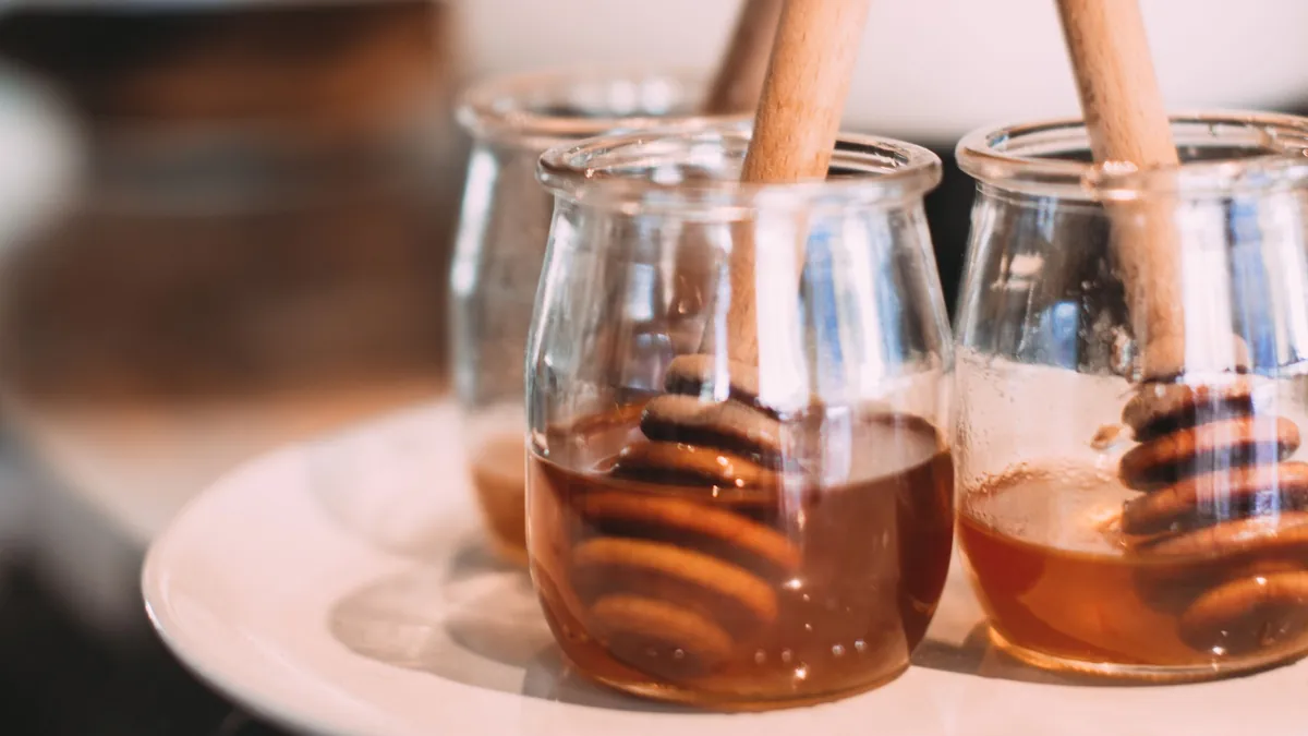 Small glass jars of honey with wooden honey dippers on a white plate