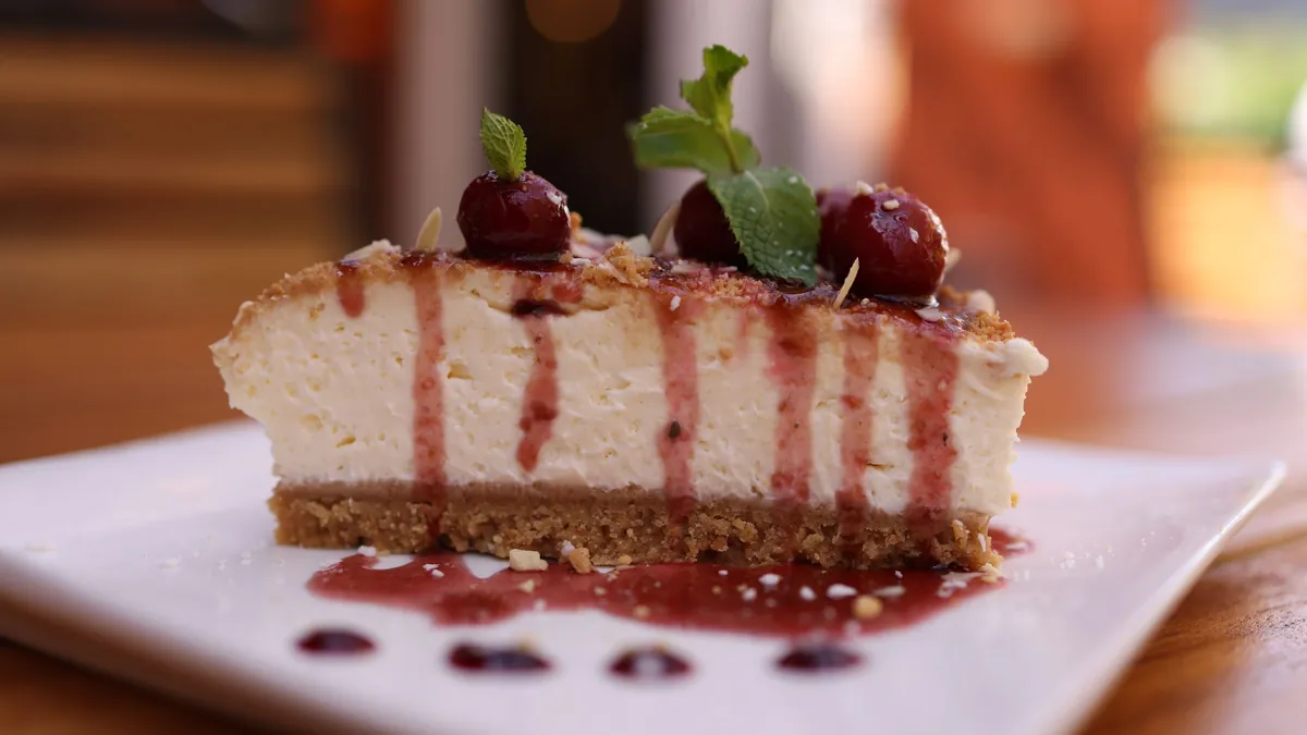 Slice of cheesecake with cherry sauce and a mint leaf on a white plate