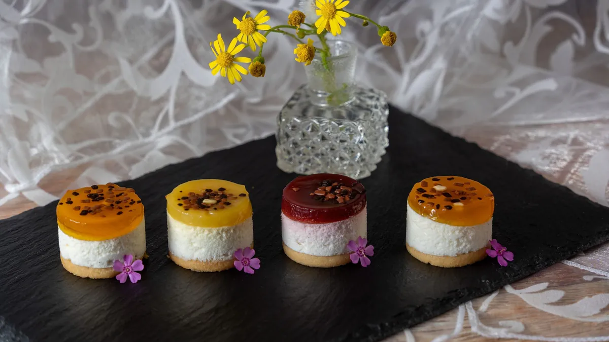 Four mini fruit cheesecakes on a slate board next to a small vase of yellow flowers