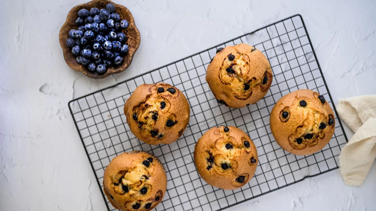 Blueberry muffins cooling on a wire rack beside a bowl of blueberries