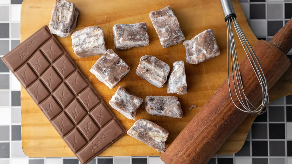 Chocolate bar and pieces of fudge on a wooden board with a whisk and rolling pin
