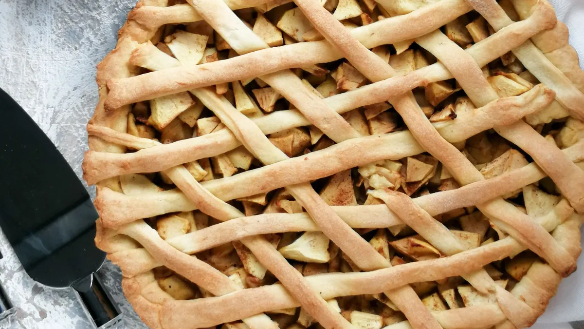 Lattice-top apple pie with fresh apples beside it