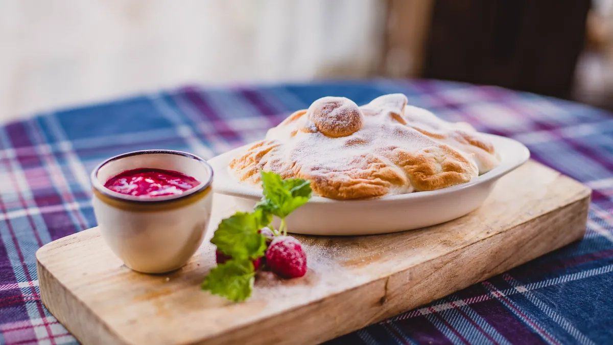 Baked dessert dusted with sugar on a wooden board beside a cup of berry sauce