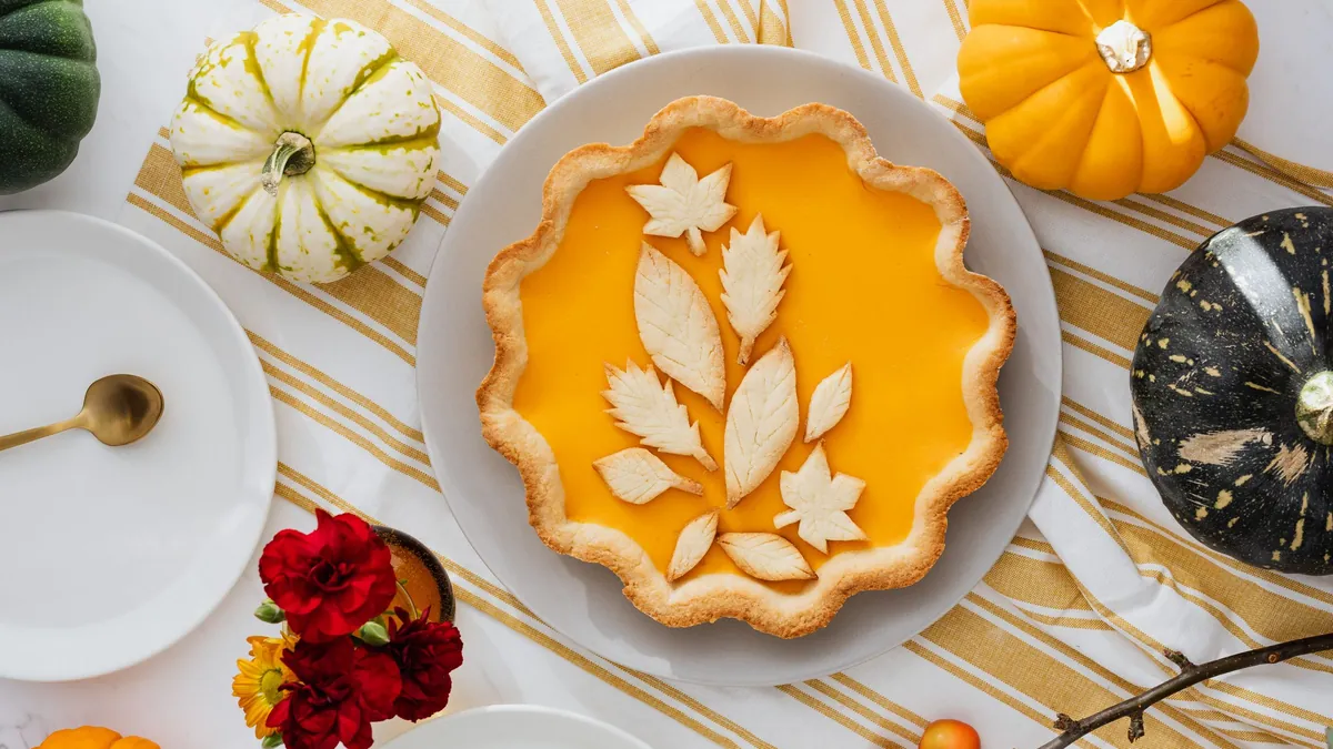 Pumpkin pie with a leaf-shaped pastry decoration on a plate surrounded by small pumpkins