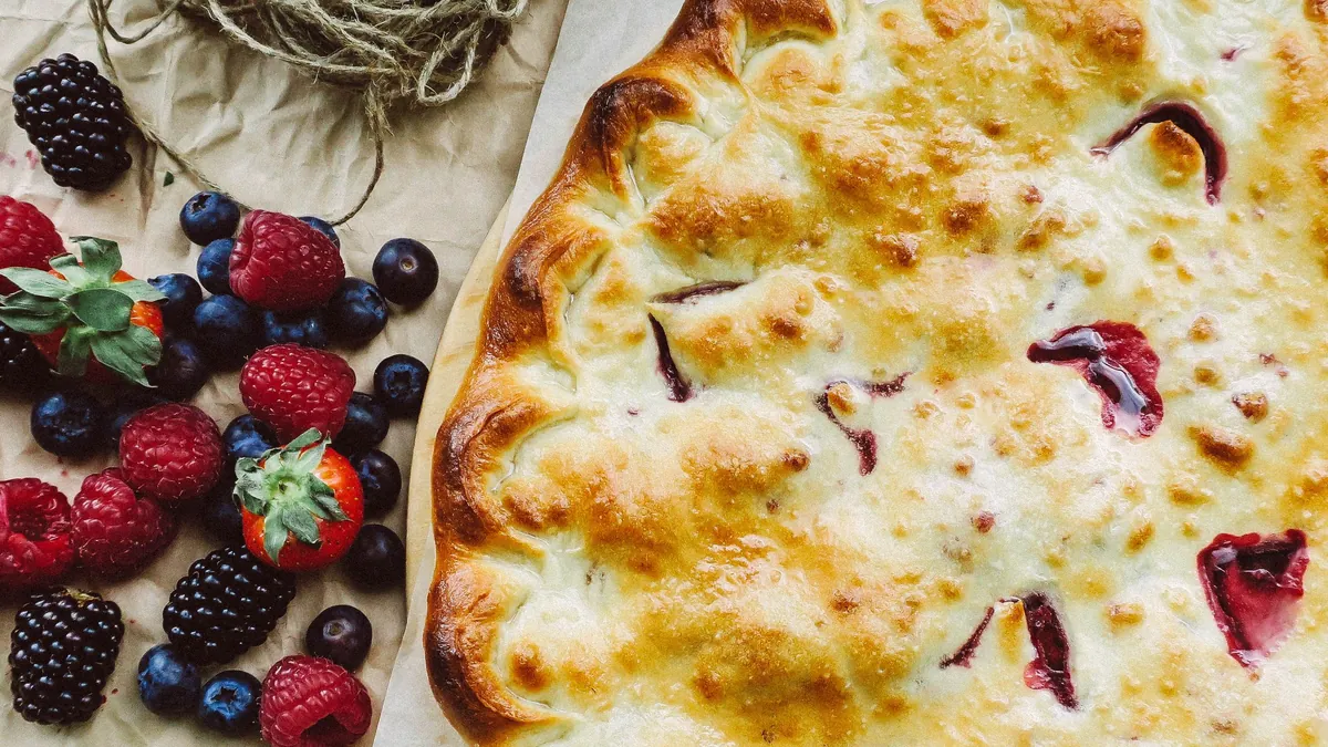 Golden berry pie next to fresh blackberries, raspberries and blueberries