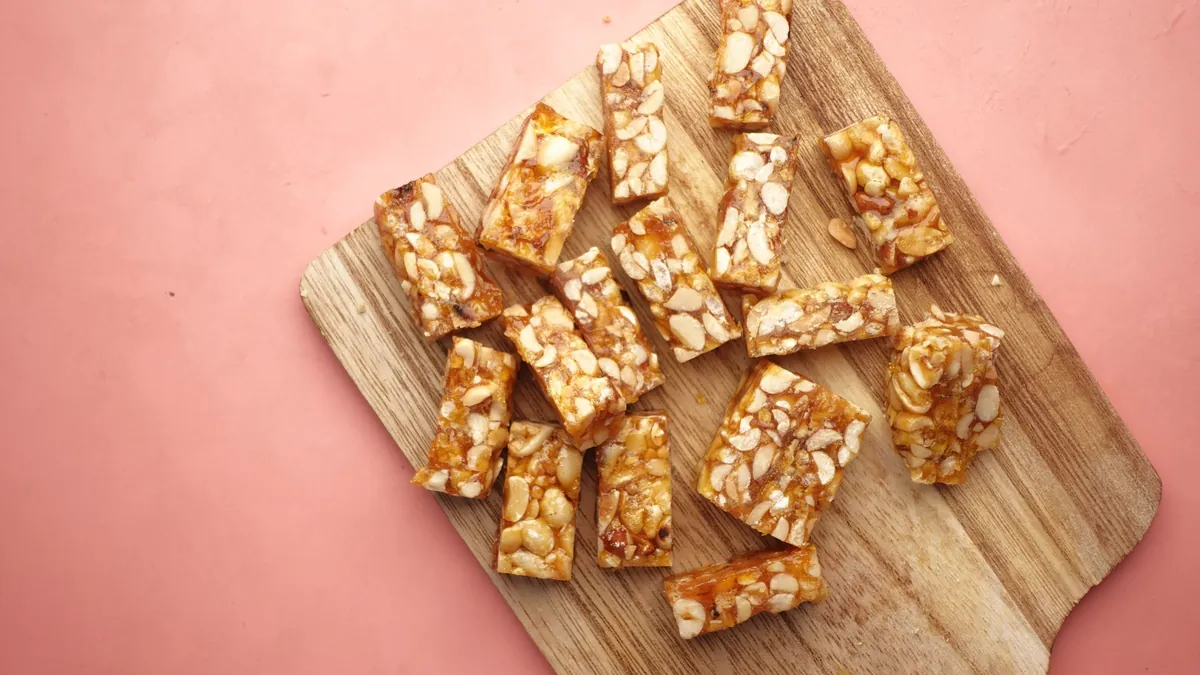 Homemade nut bars on a wooden cutting board against a pink background
