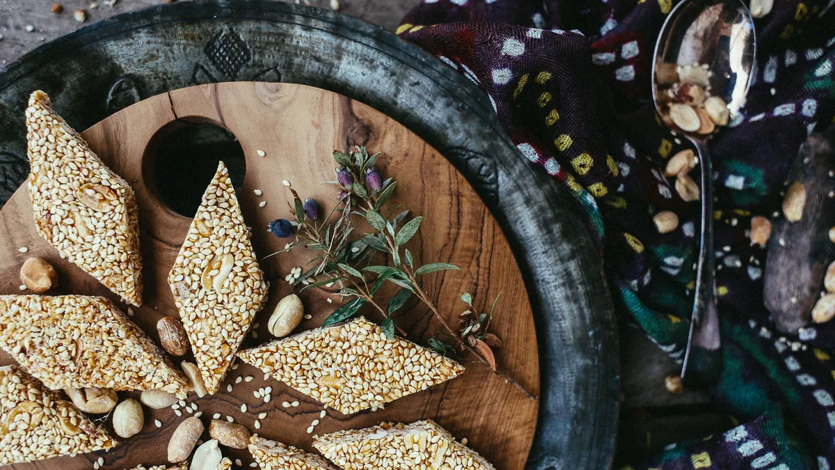 Diamond-shaped sesame and peanut brittle pieces on a wooden tray
