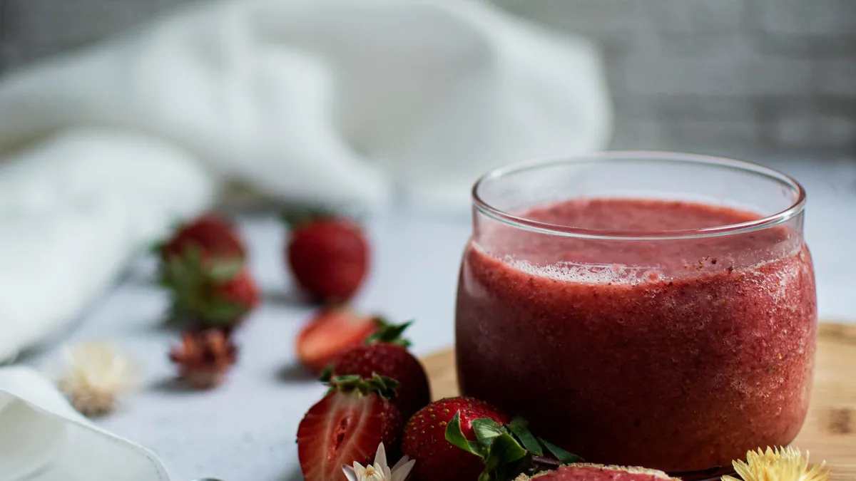 Glass jar of homemade strawberry jam with a jam-topped slice of bread and fresh strawberries