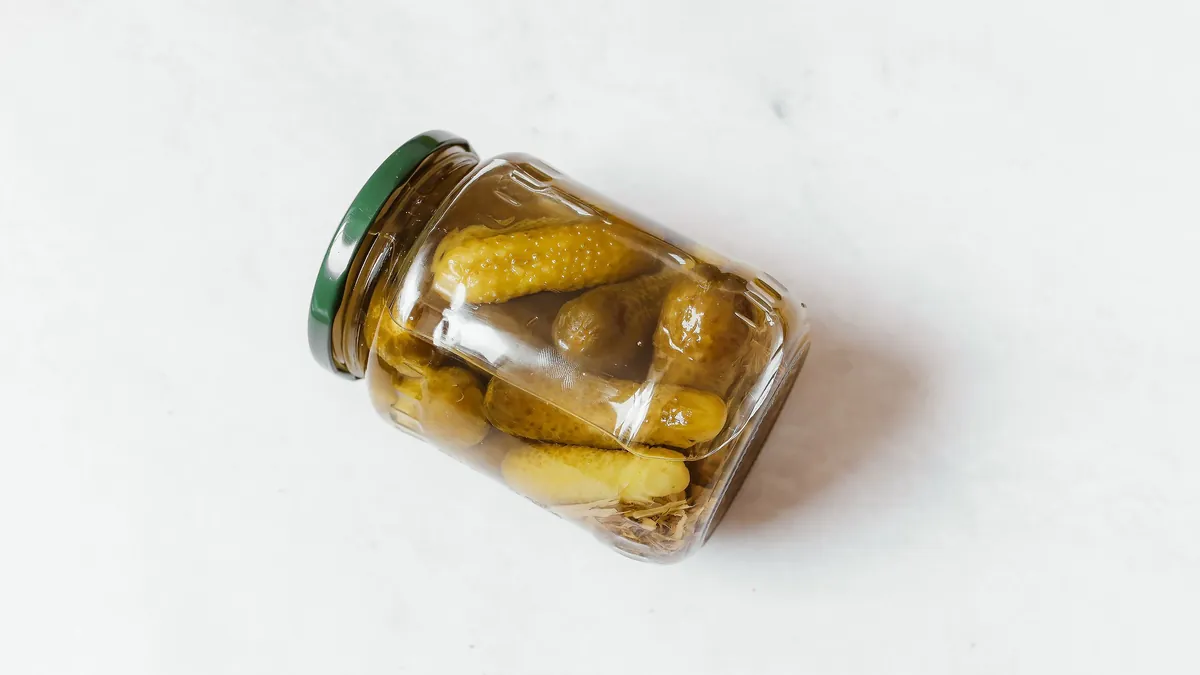 Glass jar of pickled cucumbers on a white surface
