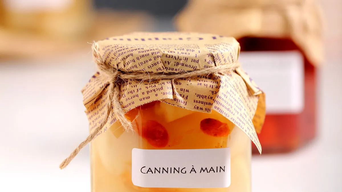 Glass jar of canned peaches with a paper lid and a handwritten-style label