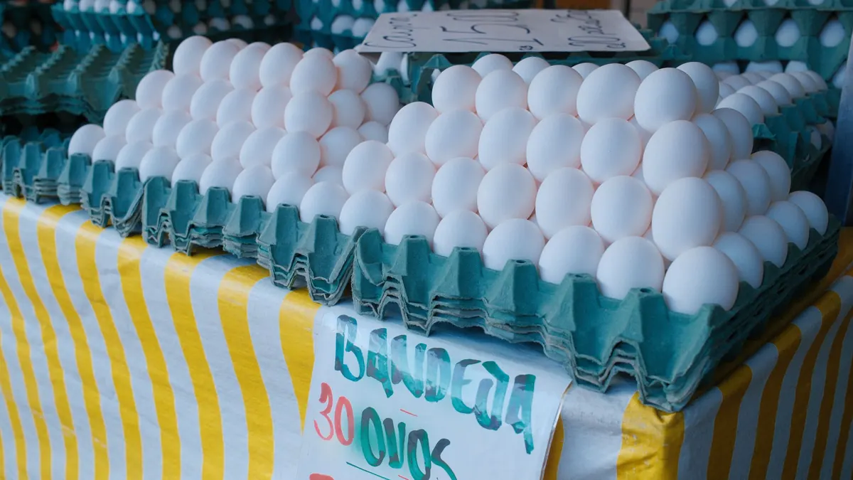 Stacked trays of white eggs on a market table with a striped cloth