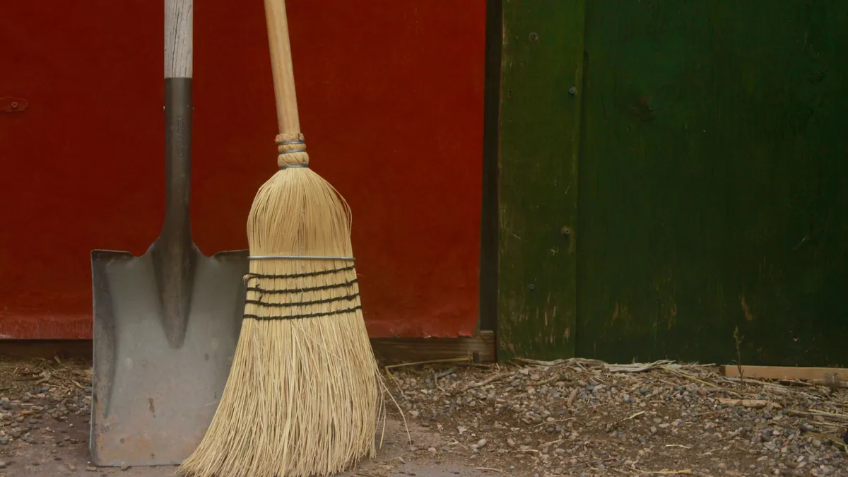 A shovel and a straw broom leaning against a red and green shed