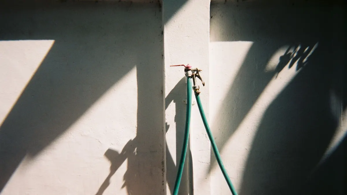 Two outdoor faucets with green hoses on a wall